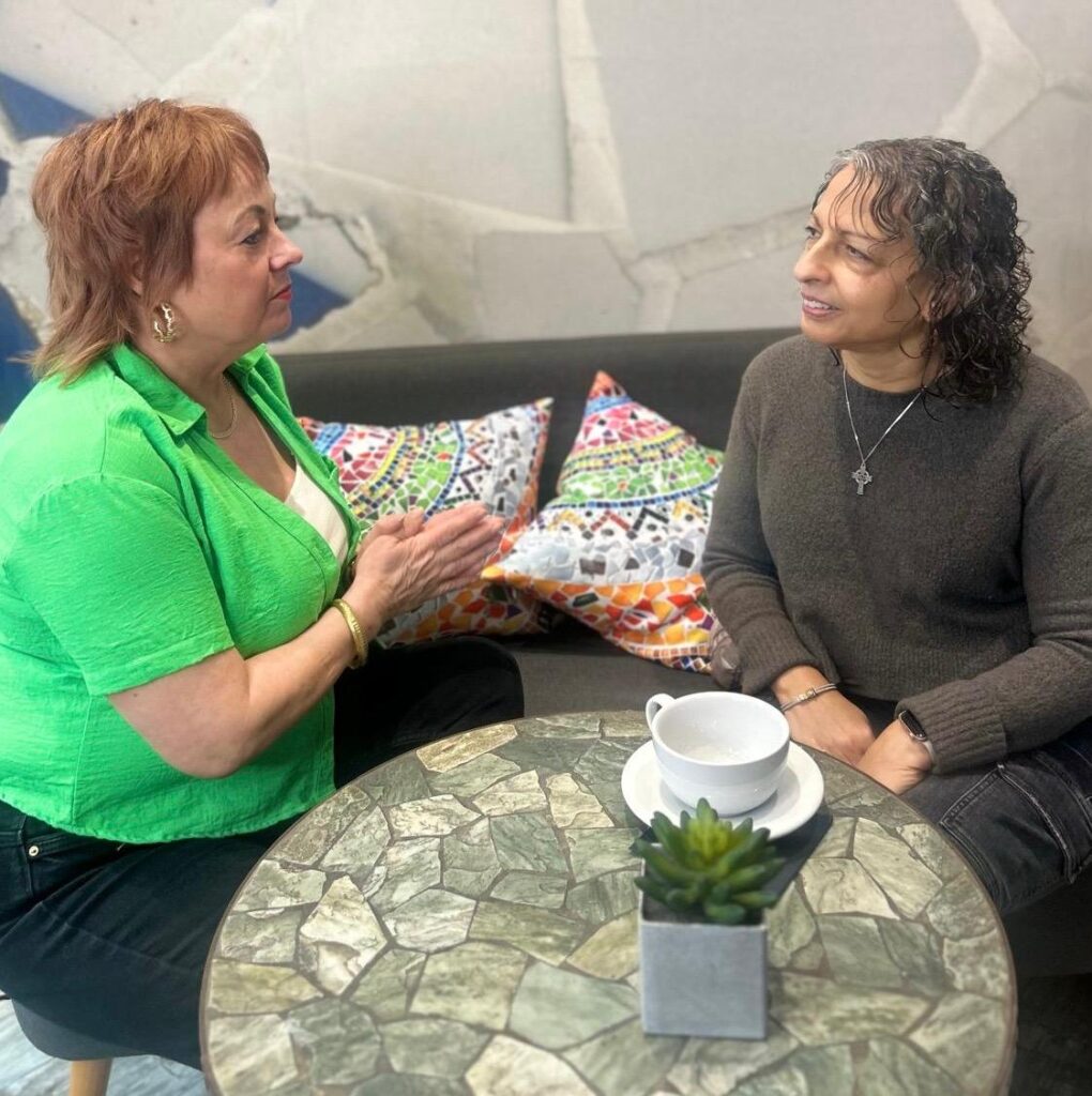 Angie sits at a coffee table, chatting to an client.
