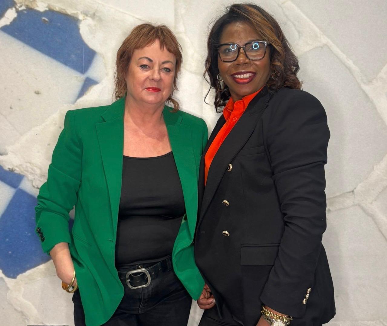 Tutors Angie and Jasmine stand side by side in front a mosaic tiled wall.